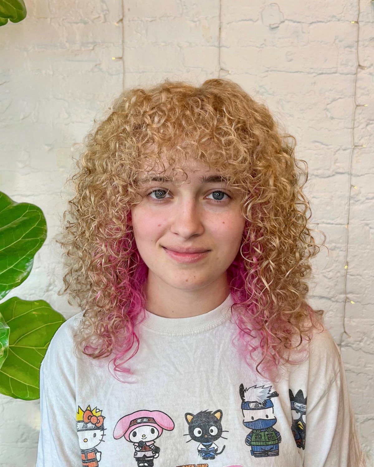 Curly blonde hair with pink lower sections frames a person in a graphic T-shirt