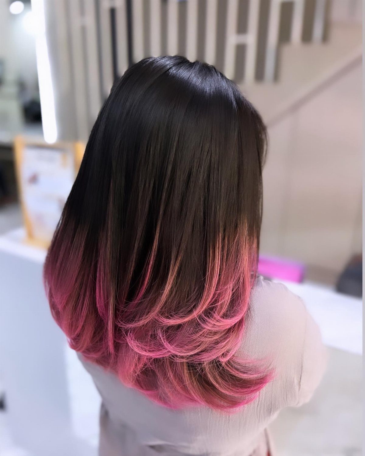 Dark straight hair fades into vivid rouge pink curled tips against a salon background