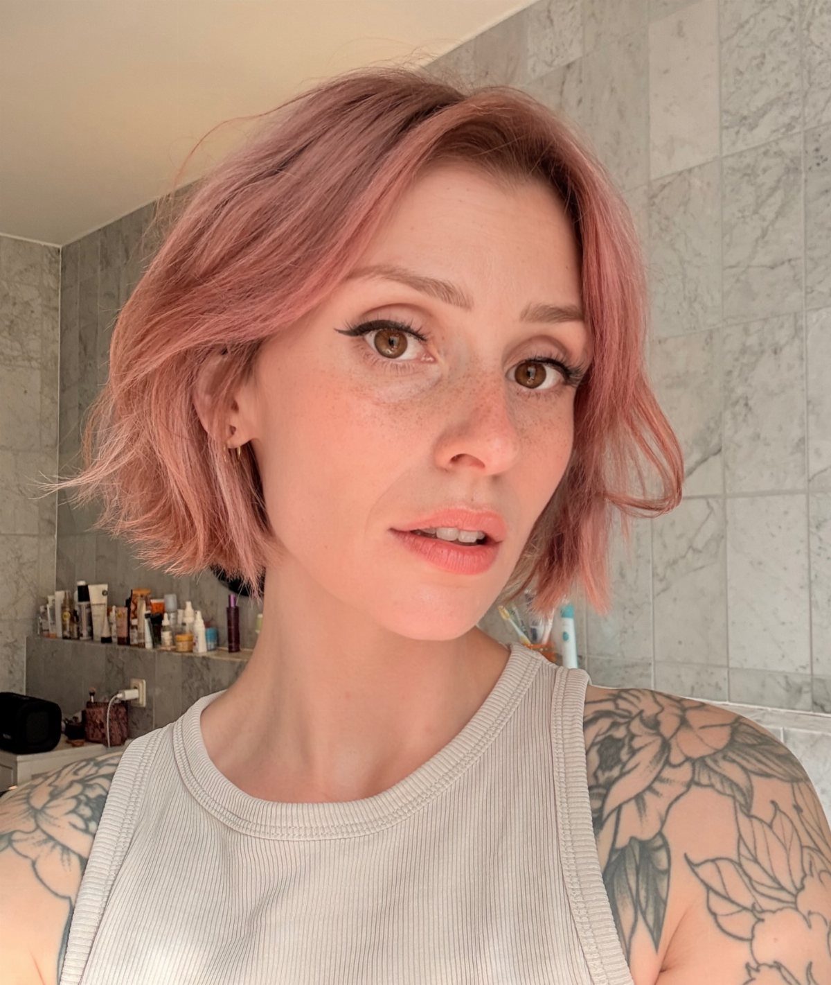 Pink-lavender textured bob frames a person’s face against pale tiled walls