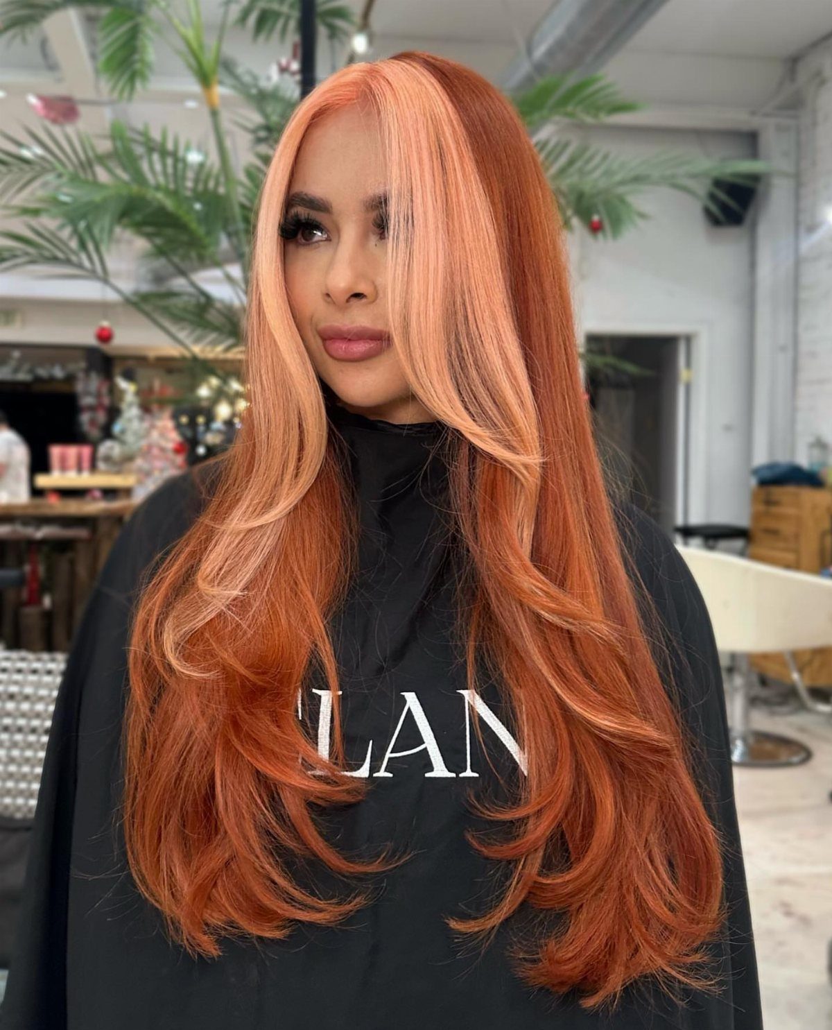 Long layered coral-red hair with pale face-framing sections in a salon
