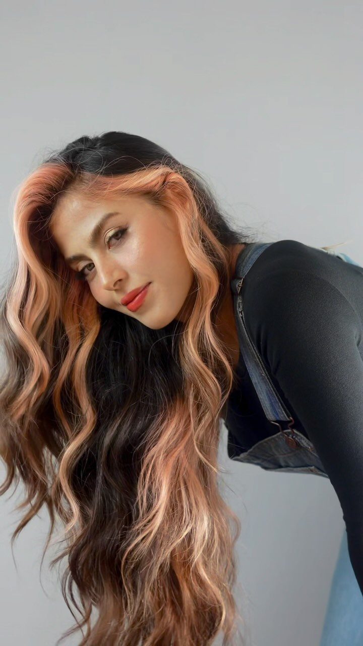 Woman with long dark waves and peach streaks framing her face