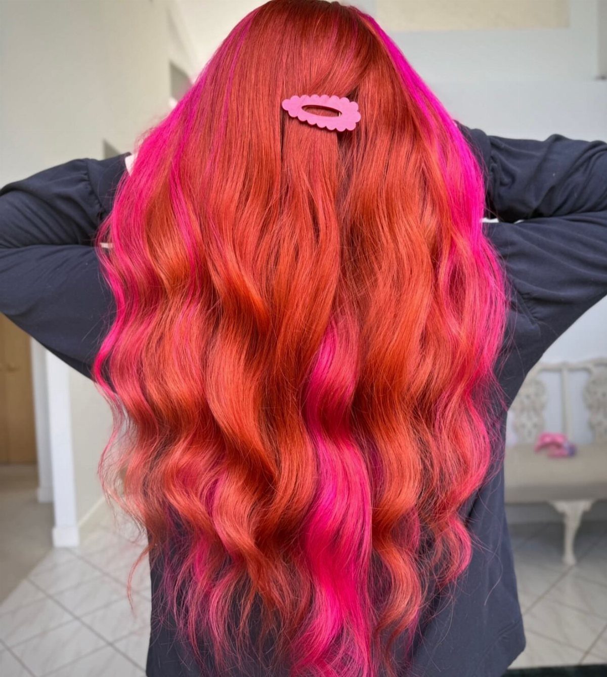 Wavy copper-red hair with vivid hot-pink streaks and a pink clip