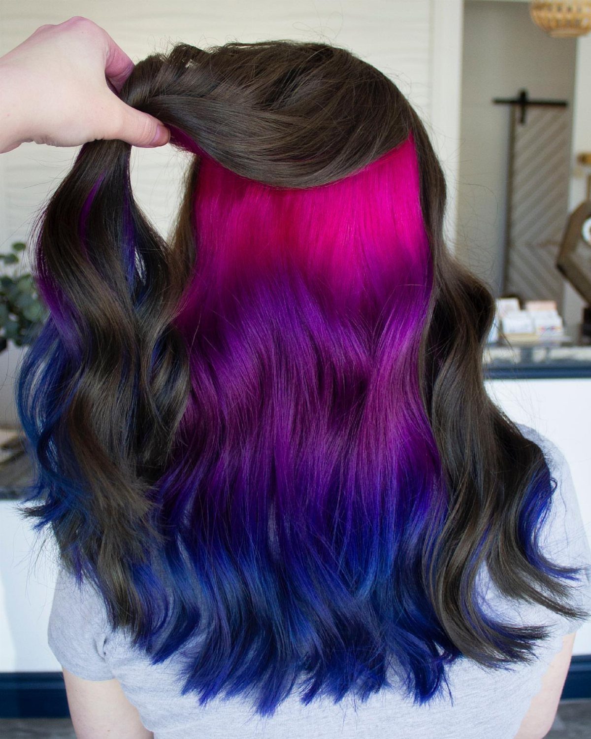 Dark wavy hair lifted to reveal vivid magenta, purple, and blue underlayers