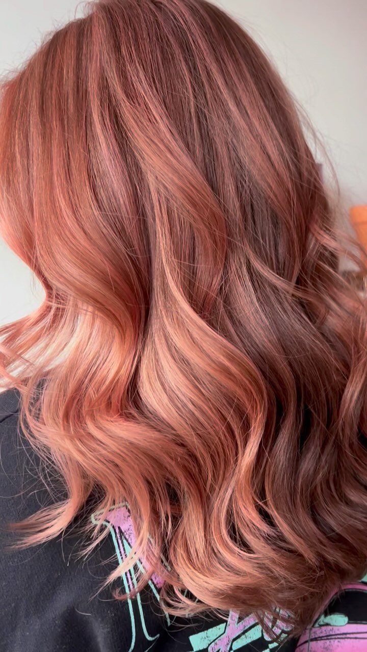 Long wavy hair showing a glossy rose gold metallic fade from dark roots