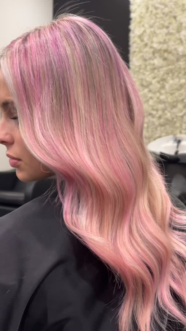 Long wavy pale pink and blonde hair with darker roots in a salon