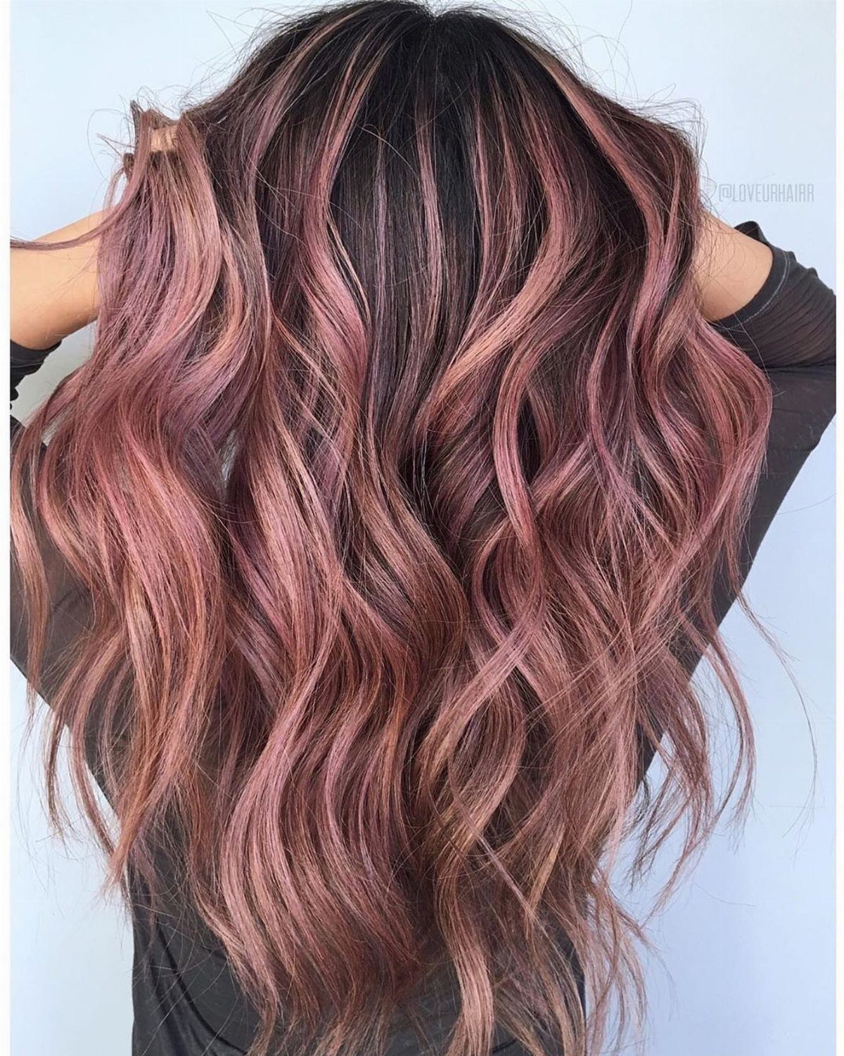 Long layered waves blend dark roots with subtle rose-pink balayage