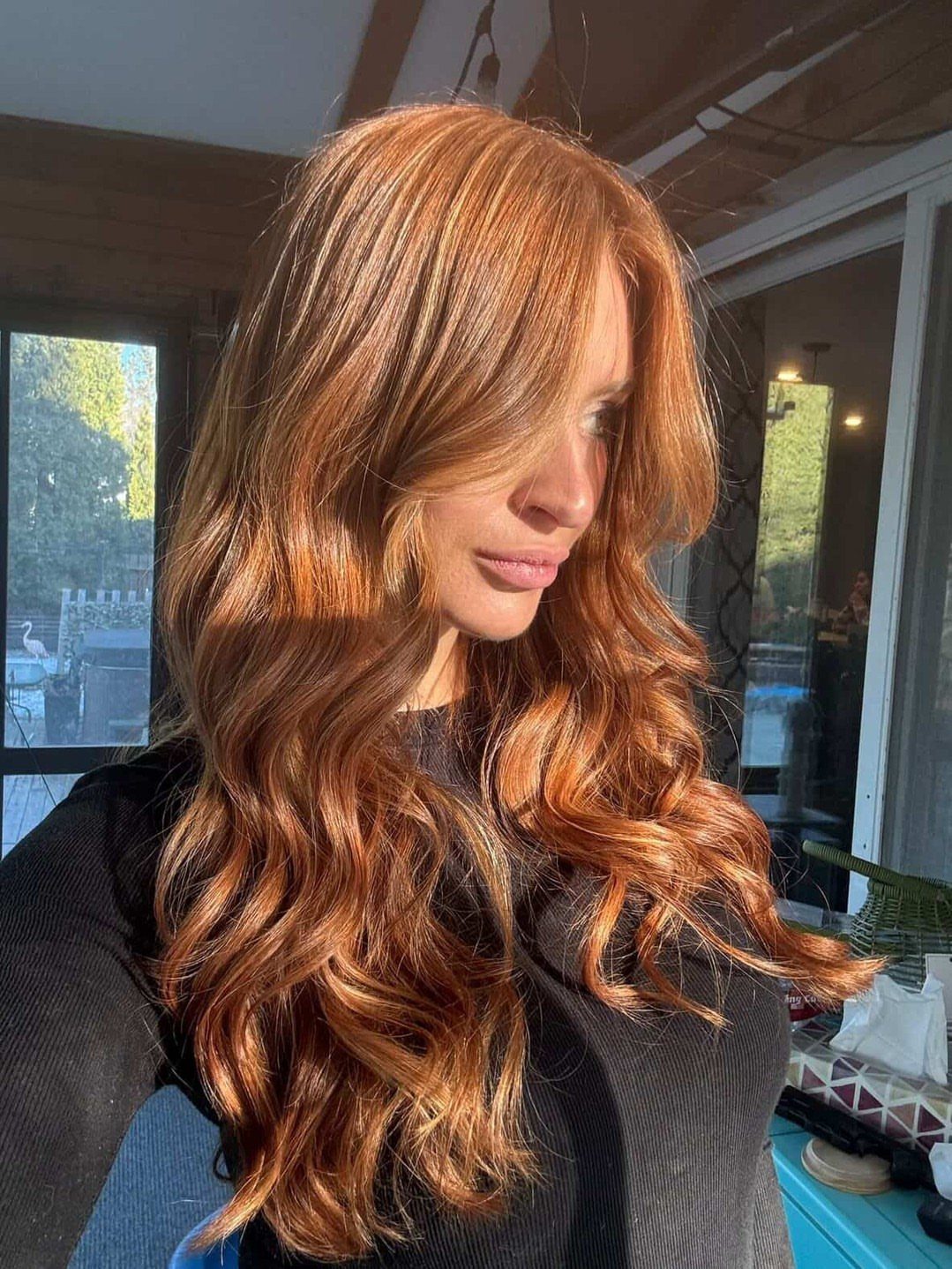 Woman with long auburn curls and lighter copper highlights by a window