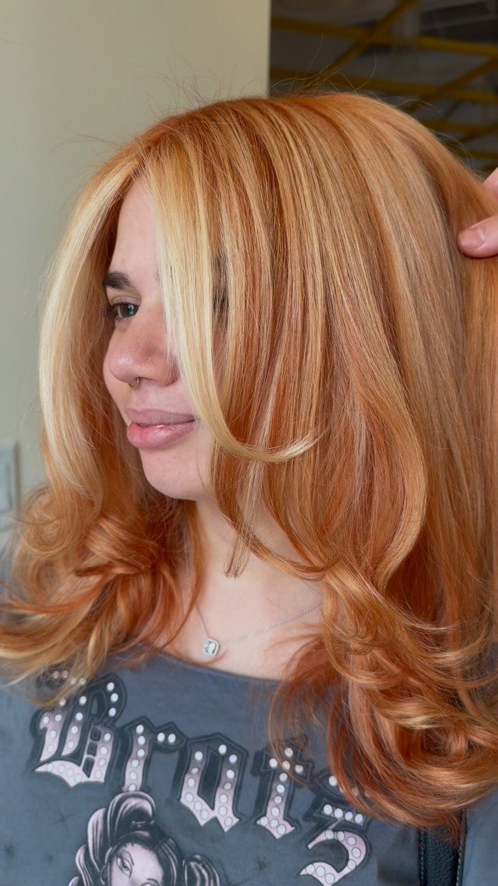 Woman displaying long blonde hair with reddish copper highlights and curled ends