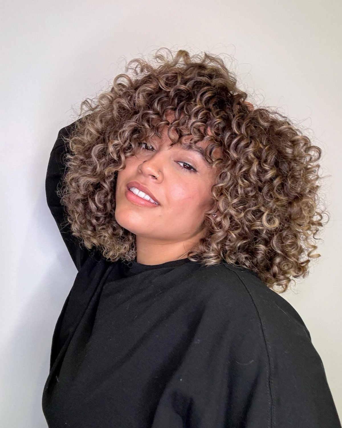 Woman with cropped curly hair showing bronze highlights against dark roots