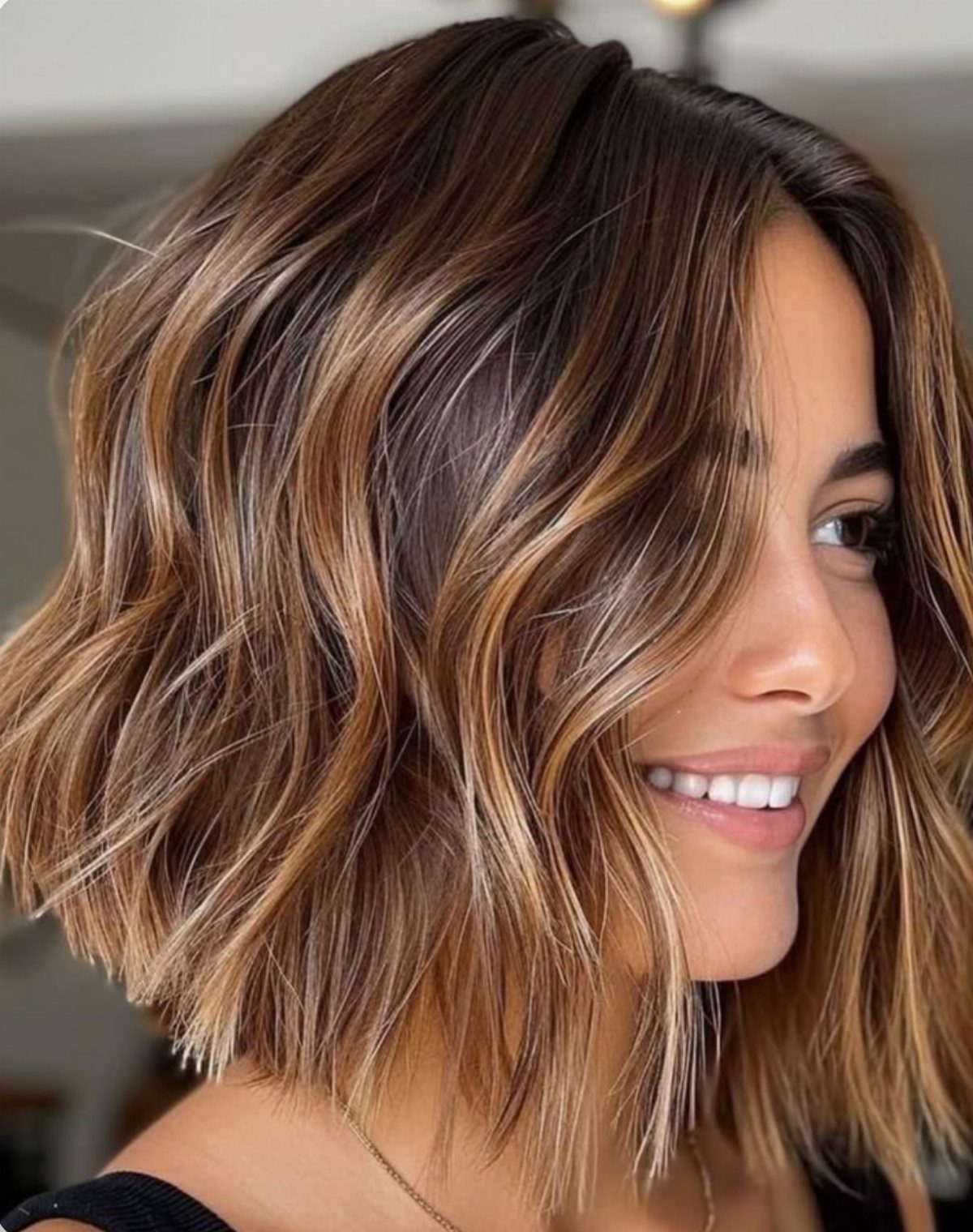 Short wavy brown bob with warm butterscotch balayage framing a smiling woman's face