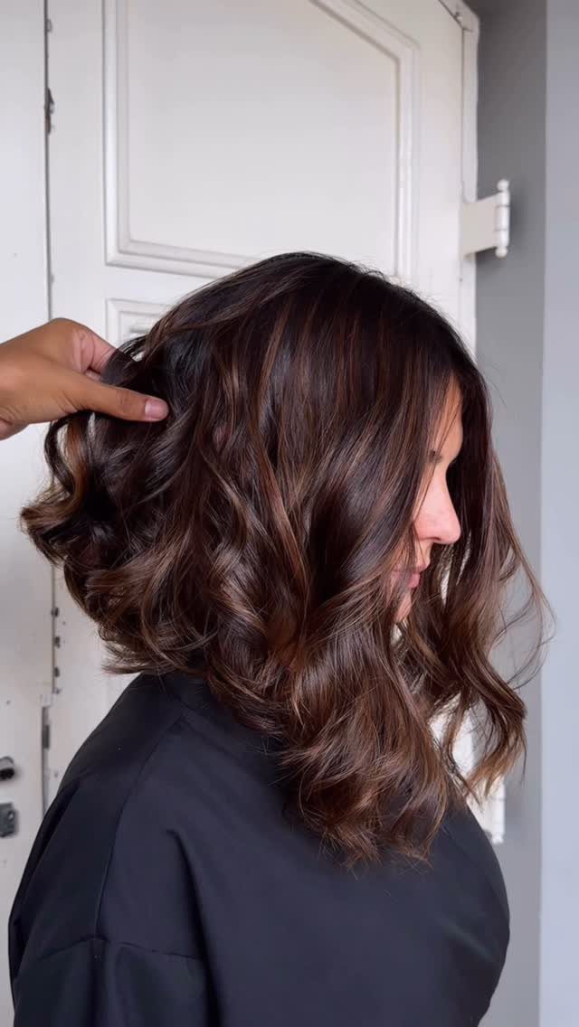 Shoulder-length dark brown curls show warm chocolate balayage highlights