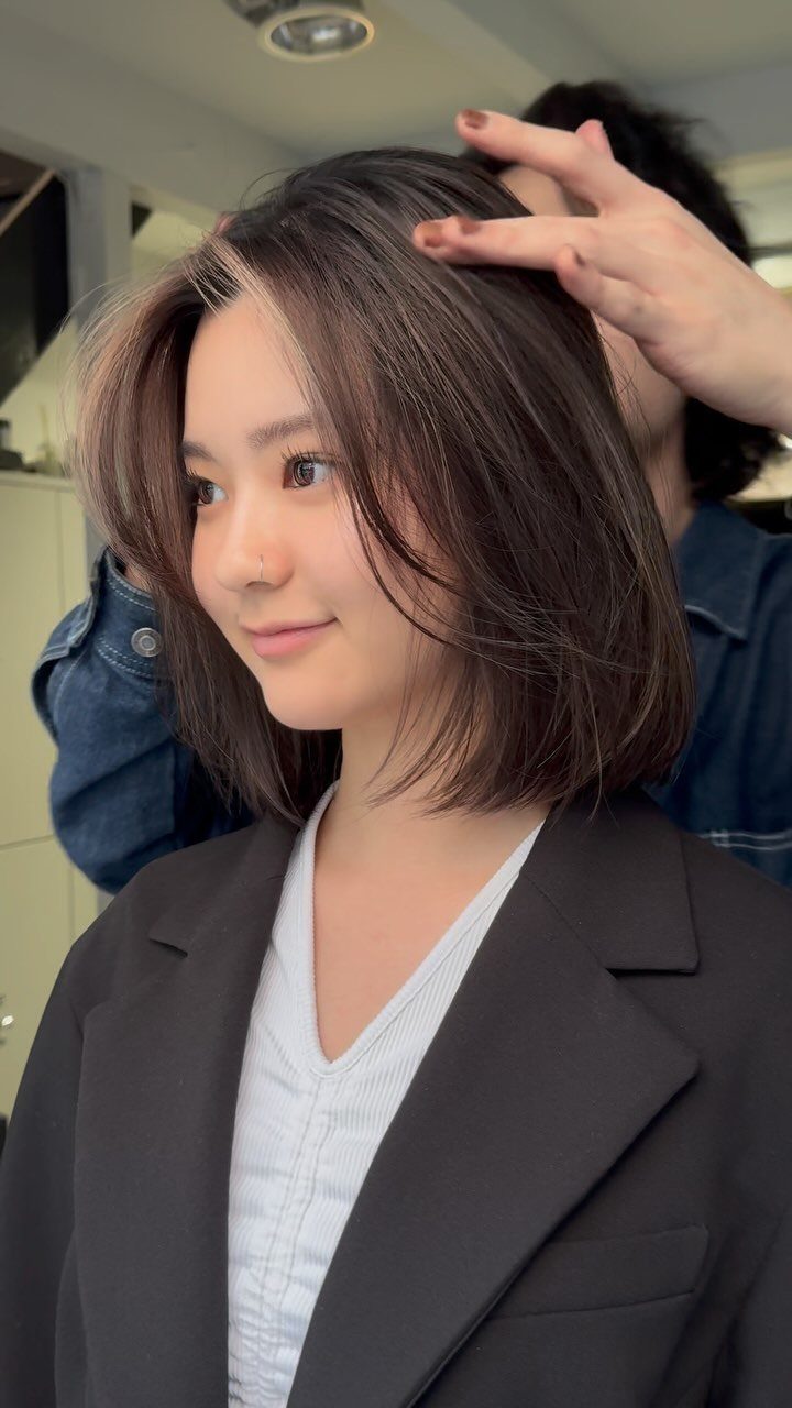 Short dark brown bob with lighter face-framing highlights in a salon