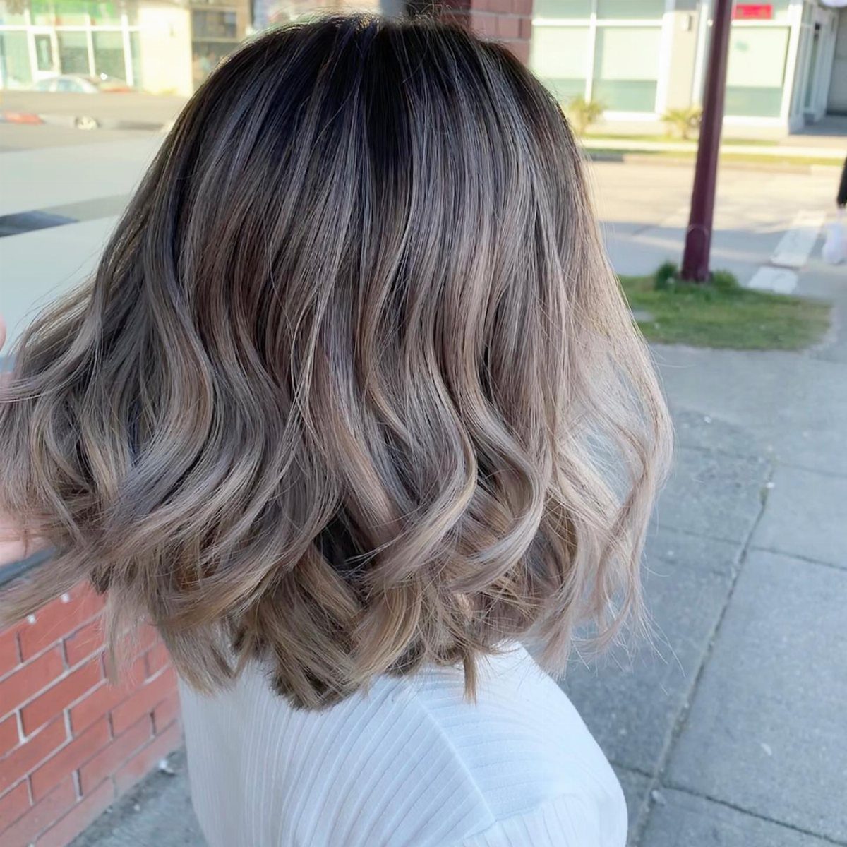 Shoulder-length wavy hair showing dark roots fading into lighter blonde ends