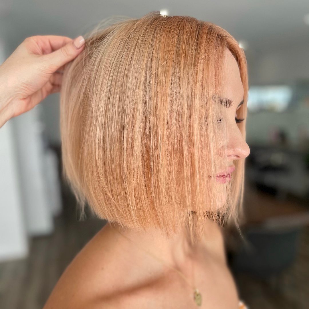 Peach-blonde bob with subtle pink tones shown in profile at a salon