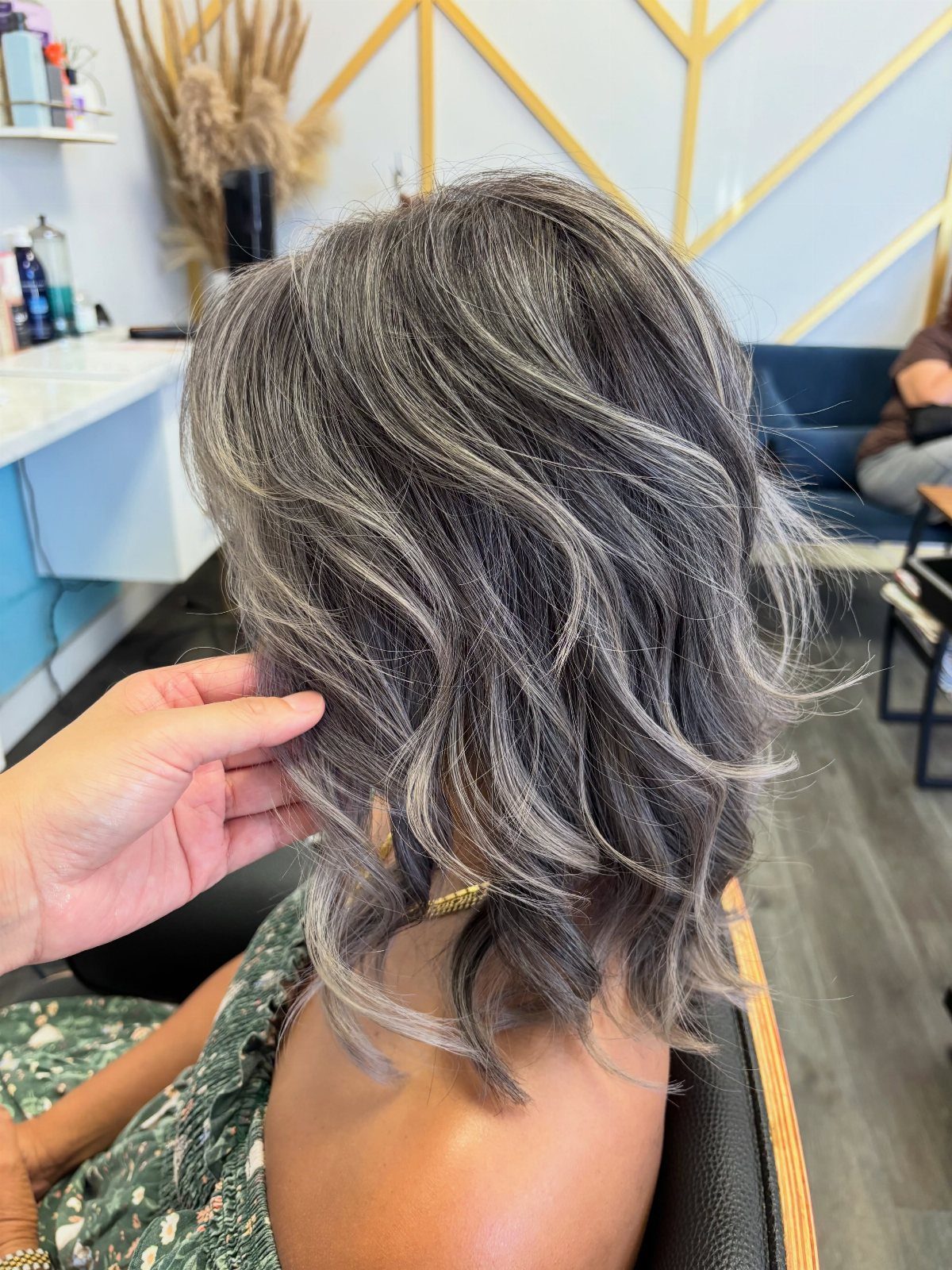 Short wavy dark hair with silver balayage highlights lifted by a hand in a salon