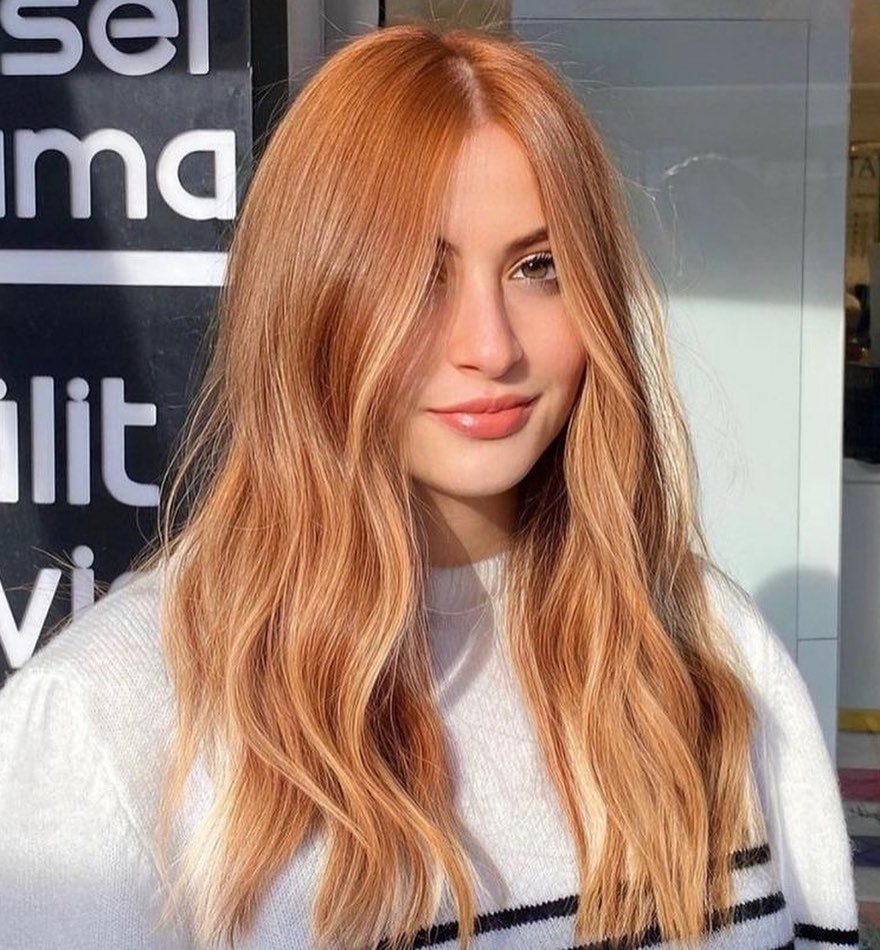 Woman with long wavy strawberry-blonde hair and golden highlights