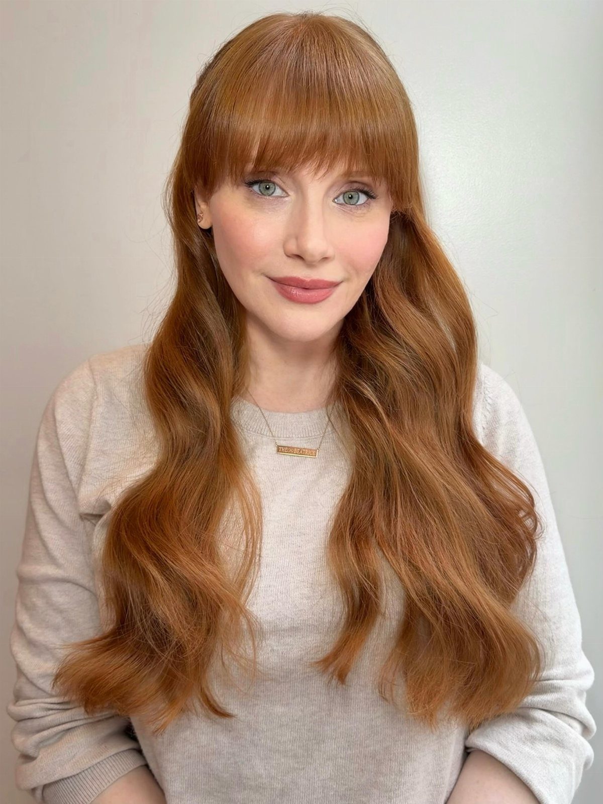 Woman with long glossy strawberry-copper hair, straight bangs, and softly curled ends